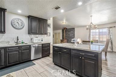 kitchen with a wood stove, dishwasher, a notable chandelier, decorative light fixtures, and a kitchen island