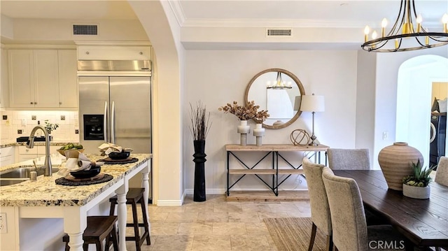 kitchen with light stone countertops, backsplash, sink, an inviting chandelier, and white cabinets