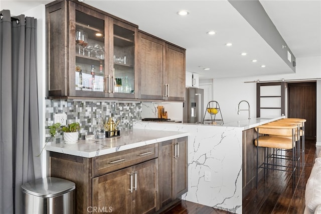 kitchen with light stone countertops, a barn door, dark hardwood / wood-style flooring, high quality fridge, and a breakfast bar area