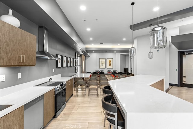 kitchen with wall chimney exhaust hood, appliances with stainless steel finishes, hanging light fixtures, and light hardwood / wood-style flooring