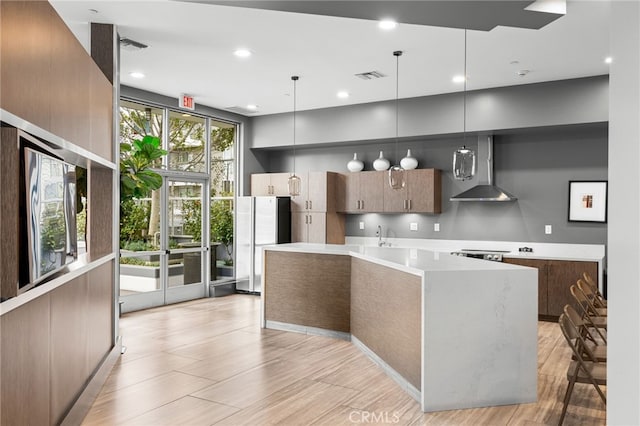 kitchen with hanging light fixtures, wall chimney range hood, and light hardwood / wood-style floors