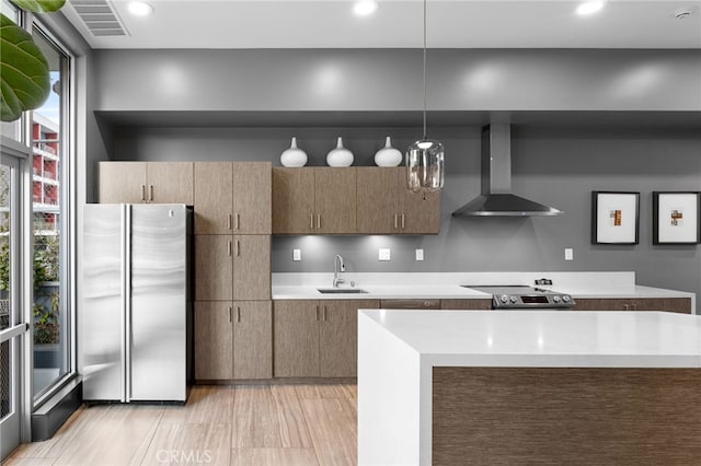 kitchen with light hardwood / wood-style flooring, stainless steel appliances, sink, wall chimney exhaust hood, and decorative light fixtures