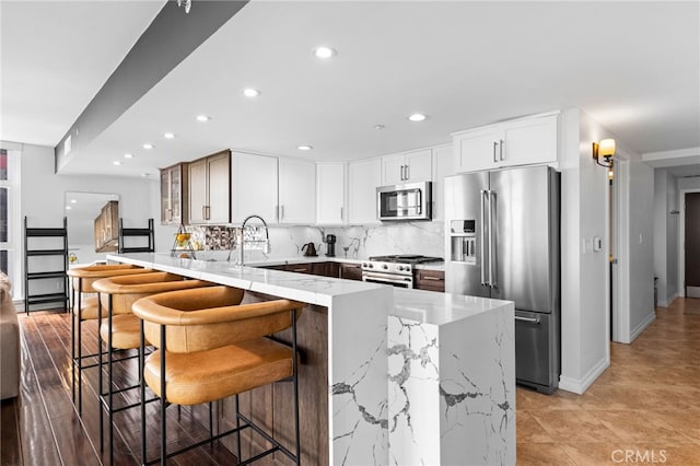 kitchen featuring high end appliances, a kitchen bar, white cabinetry, light stone counters, and tasteful backsplash