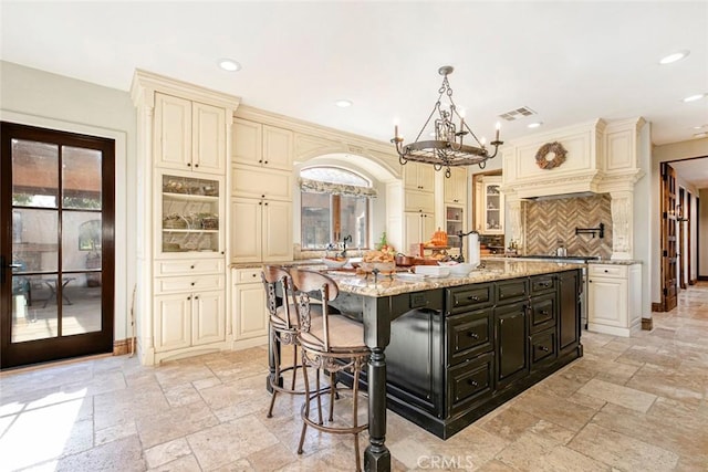 kitchen with cream cabinetry, an island with sink, a wealth of natural light, and tasteful backsplash