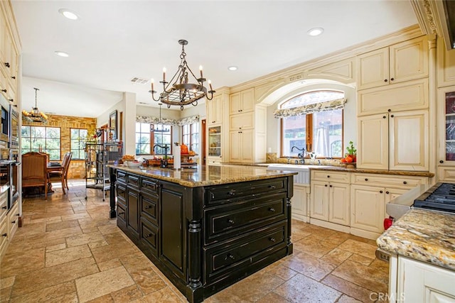 kitchen with cream cabinetry, light stone countertops, hanging light fixtures, and a wealth of natural light