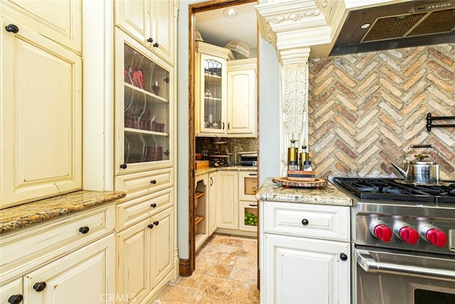 kitchen with light stone countertops, tasteful backsplash, custom exhaust hood, high end stainless steel range, and cream cabinetry