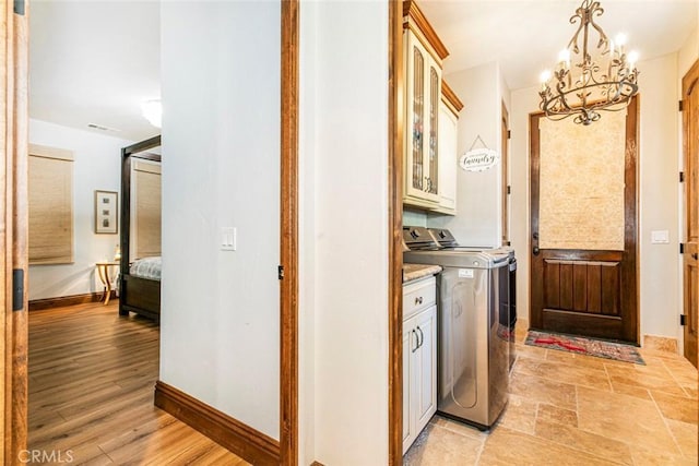 laundry room featuring cabinets, light wood-type flooring, a chandelier, and washer and dryer