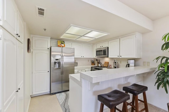 kitchen featuring tile countertops, stainless steel appliances, kitchen peninsula, and white cabinets