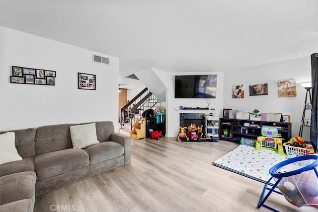 living area with wood finished floors, visible vents, a premium fireplace, and stairs