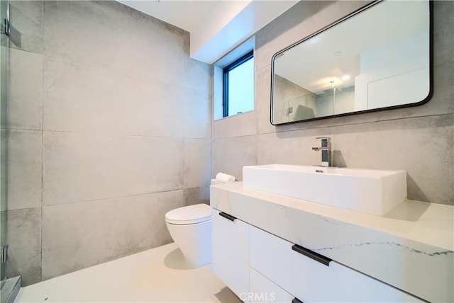 bathroom featuring vanity, toilet, a shower with door, and tile walls