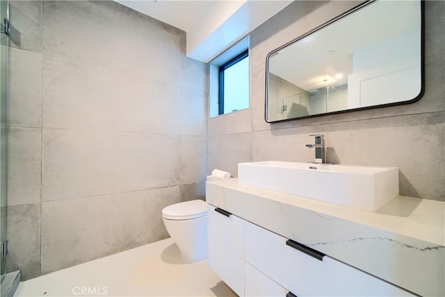 bathroom featuring a shower with door, vanity, tile walls, and toilet