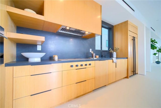 kitchen featuring backsplash, built in refrigerator, light brown cabinetry, and cooktop