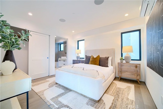 bedroom featuring a wall mounted AC, ensuite bathroom, and light hardwood / wood-style flooring