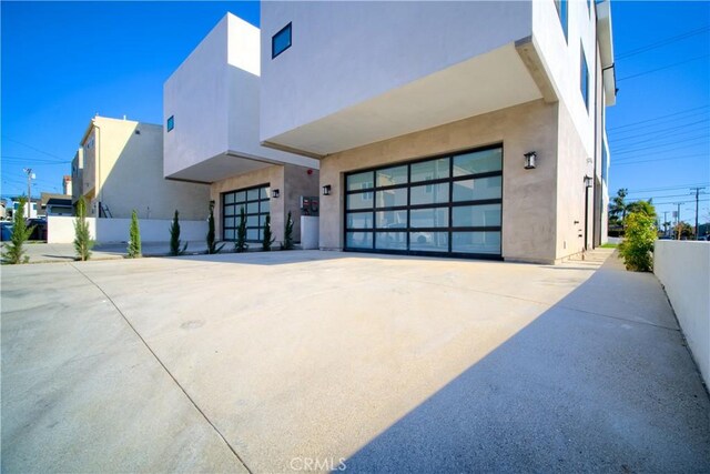 view of property exterior featuring an attached garage, driveway, stucco siding, and fence