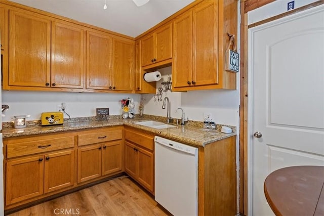 kitchen with dishwasher, light stone counters, light wood-type flooring, and sink