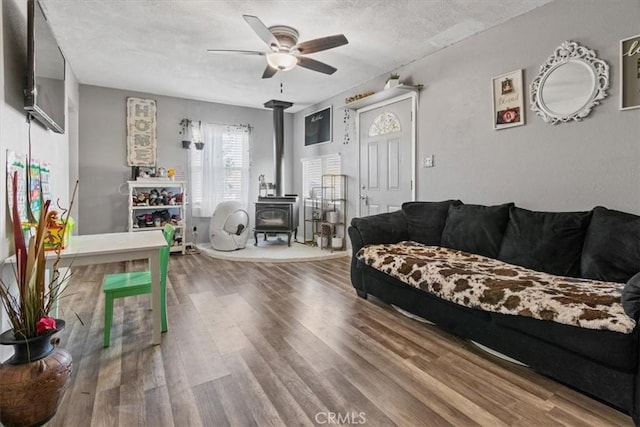 living room with hardwood / wood-style floors, ceiling fan, a wood stove, and a textured ceiling