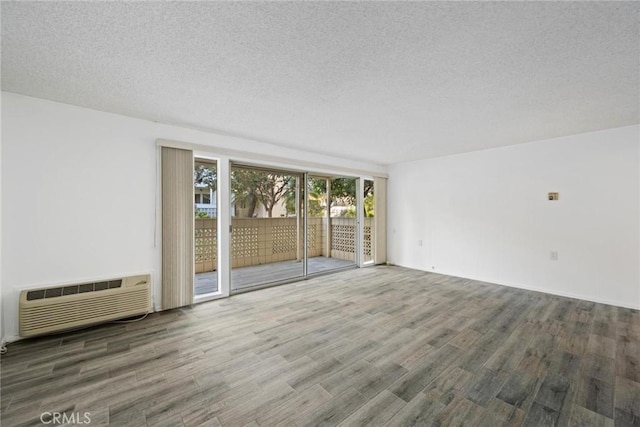 spare room featuring hardwood / wood-style floors, an AC wall unit, and a textured ceiling