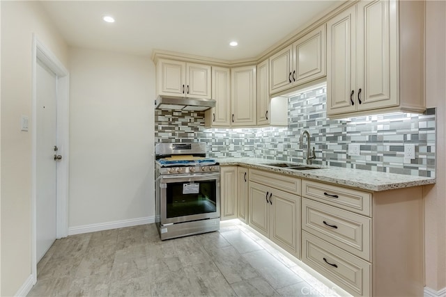 kitchen with light stone countertops, sink, cream cabinetry, stainless steel range oven, and light hardwood / wood-style flooring