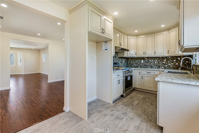 kitchen with backsplash, sink, light stone countertops, light wood-type flooring, and stainless steel range oven