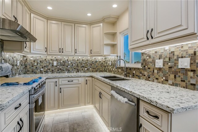 kitchen featuring decorative backsplash, cream cabinets, light stone countertops, sink, and stainless steel appliances