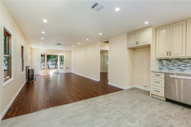 kitchen with dishwasher, cream cabinetry, backsplash, light hardwood / wood-style floors, and light stone counters