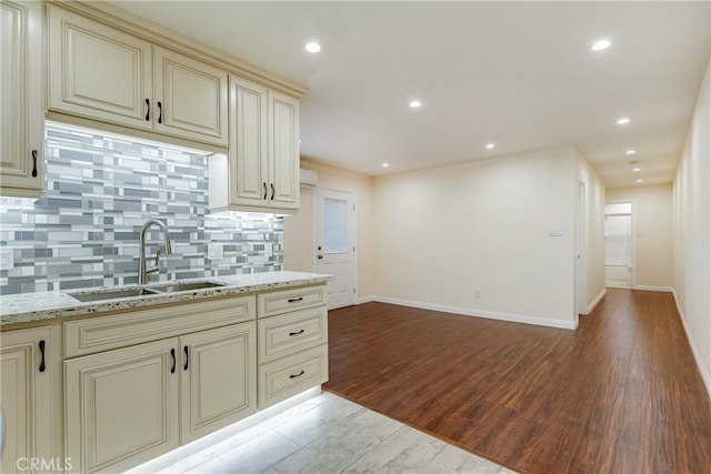 kitchen with tasteful backsplash, sink, light wood-type flooring, cream cabinetry, and light stone counters