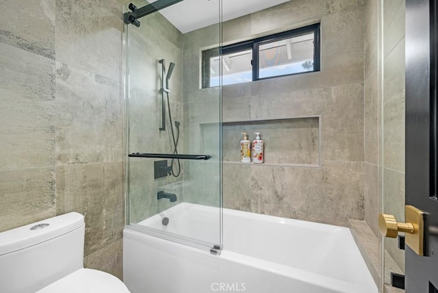 bathroom featuring toilet, tile walls, and combined bath / shower with glass door