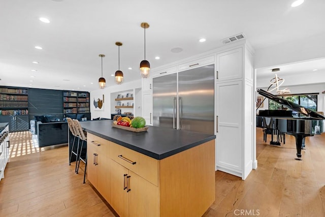 kitchen featuring stainless steel built in fridge, decorative light fixtures, a breakfast bar, a kitchen island, and light wood-type flooring