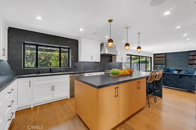 kitchen with white cabinets, light hardwood / wood-style flooring, stainless steel dishwasher, and wall chimney exhaust hood