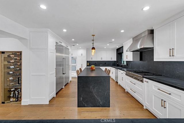 kitchen with light hardwood / wood-style floors, a center island, wall chimney range hood, and appliances with stainless steel finishes