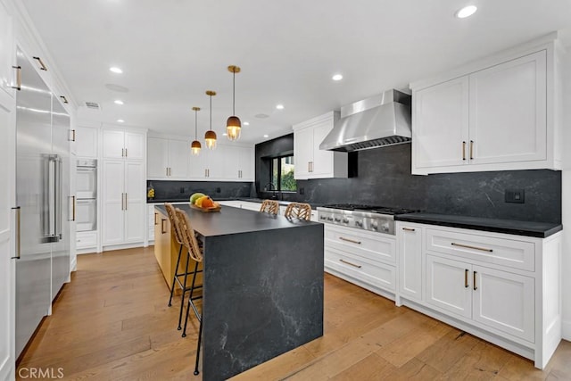 kitchen featuring a breakfast bar, wall chimney exhaust hood, light hardwood / wood-style floors, appliances with stainless steel finishes, and a kitchen island