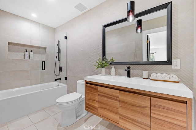 full bathroom featuring vanity, tile patterned flooring, tiled shower / bath combo, toilet, and tile walls