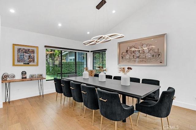 dining area with light wood-type flooring, an inviting chandelier, and lofted ceiling