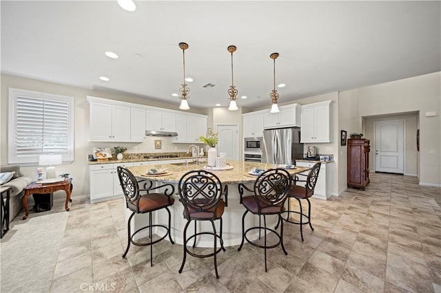 kitchen with light stone counters, decorative light fixtures, a kitchen island with sink, white cabinets, and appliances with stainless steel finishes