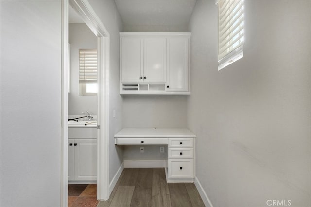 unfurnished office with dark wood-type flooring, built in desk, and sink