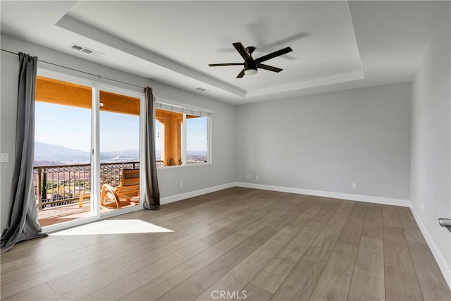 empty room with a mountain view, a raised ceiling, light wood-type flooring, and ceiling fan