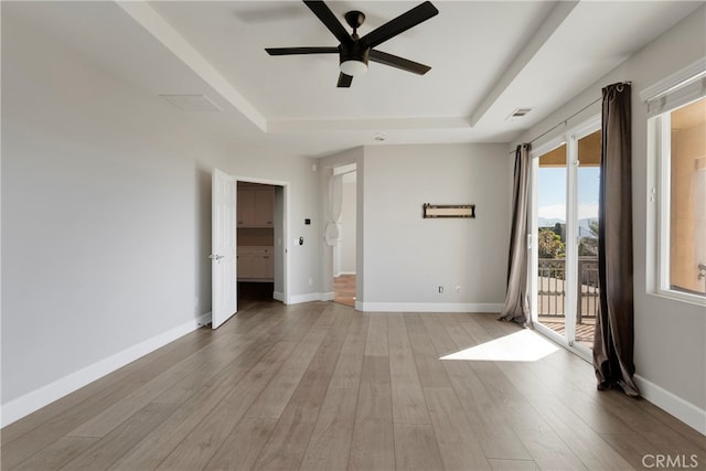 unfurnished room featuring light hardwood / wood-style floors, a tray ceiling, and ceiling fan