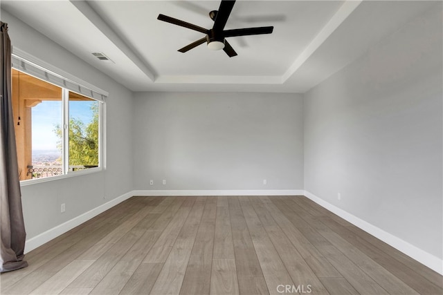 spare room featuring ceiling fan, light wood-type flooring, and a raised ceiling