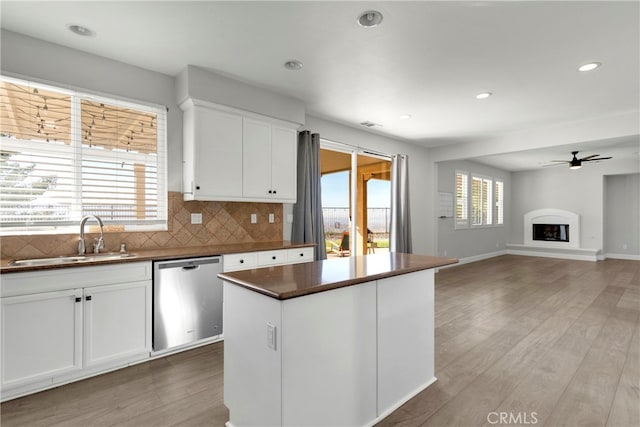 kitchen with wood-type flooring, sink, a kitchen island, stainless steel dishwasher, and white cabinets