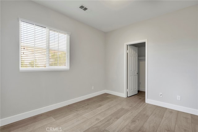 unfurnished bedroom featuring a spacious closet, a closet, and light hardwood / wood-style flooring