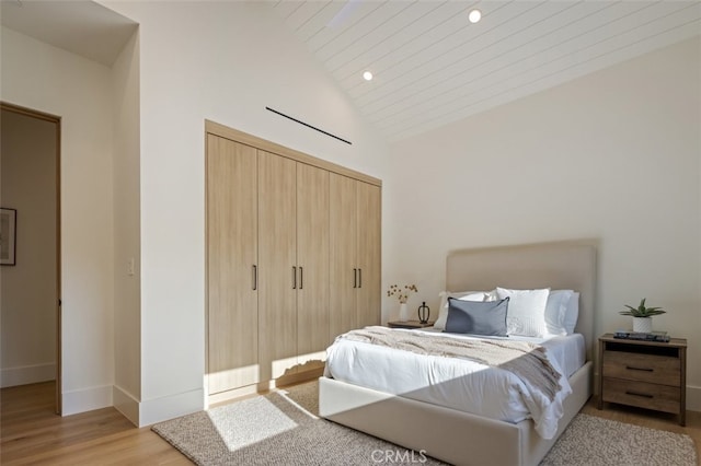 bedroom with a closet, light hardwood / wood-style floors, wood ceiling, and high vaulted ceiling