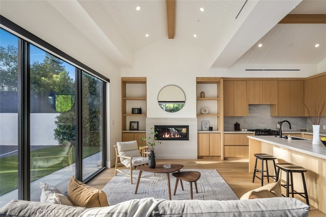 living room with sink, lofted ceiling with beams, and light hardwood / wood-style flooring