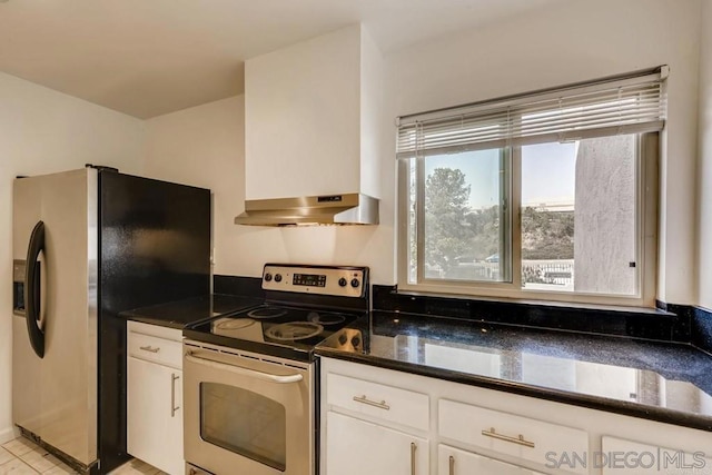 kitchen with white cabinets, wall chimney exhaust hood, dark stone countertops, and appliances with stainless steel finishes