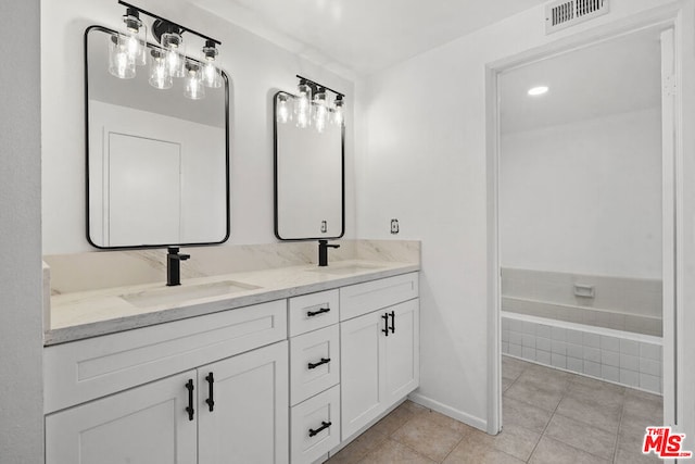 bathroom with tile patterned flooring, vanity, and tiled bath