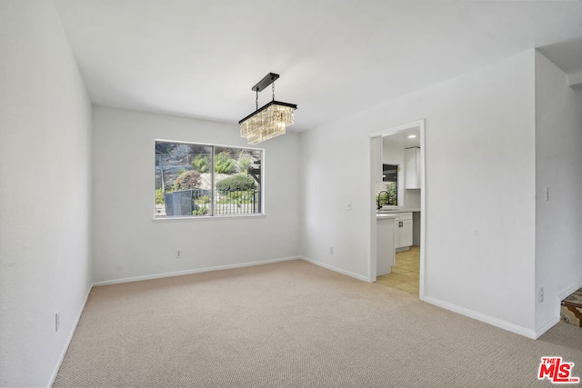 empty room with a chandelier, light colored carpet, and sink