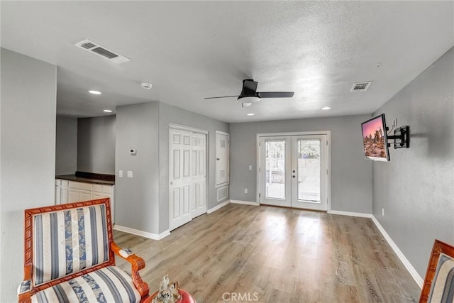 foyer entrance with french doors, ceiling fan, light hardwood / wood-style flooring, and a textured ceiling