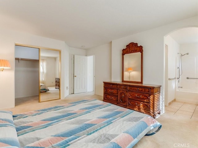 bedroom featuring ensuite bathroom, light colored carpet, and a closet