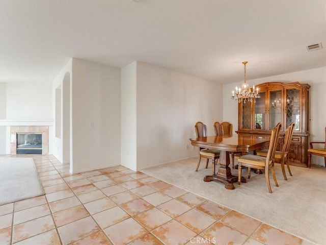 dining area with light carpet, a tile fireplace, and an inviting chandelier