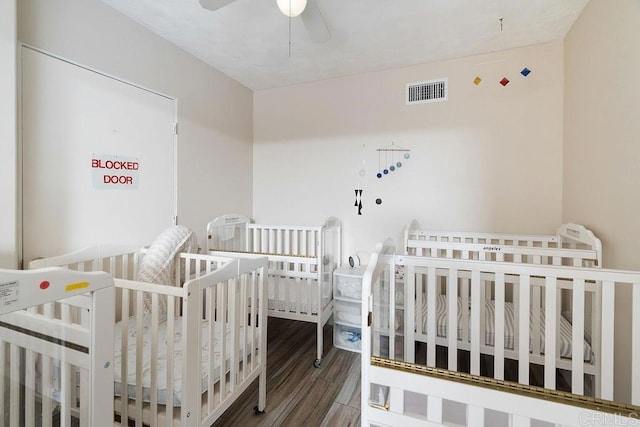 bedroom featuring wood-type flooring, a crib, and ceiling fan