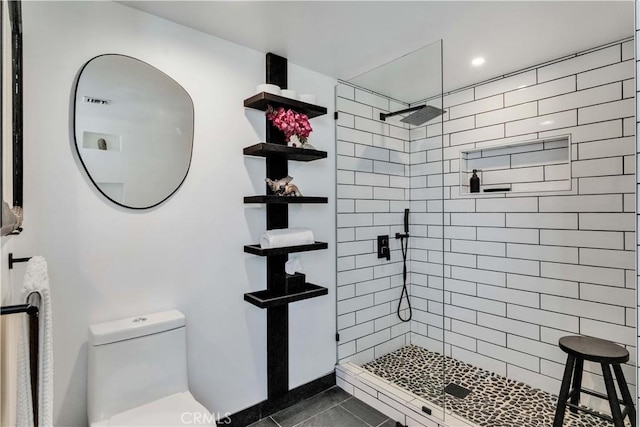 bathroom with toilet, tile patterned flooring, and tiled shower